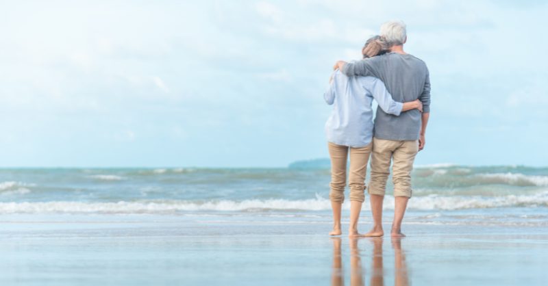 Couple embracing on the beach, while looking at the waves. 